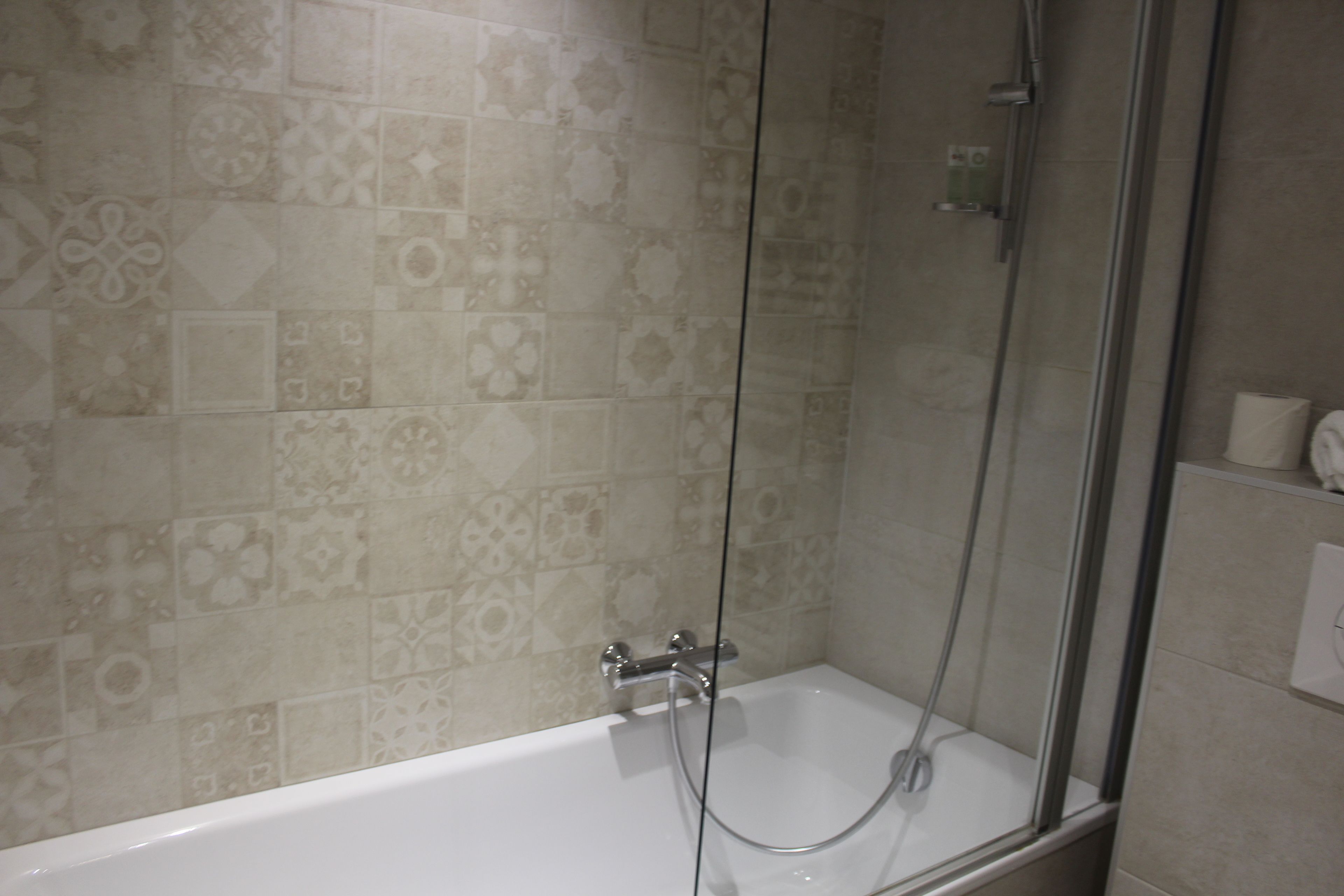 A bathroom with a bathtub, shower, and patterned tiles.