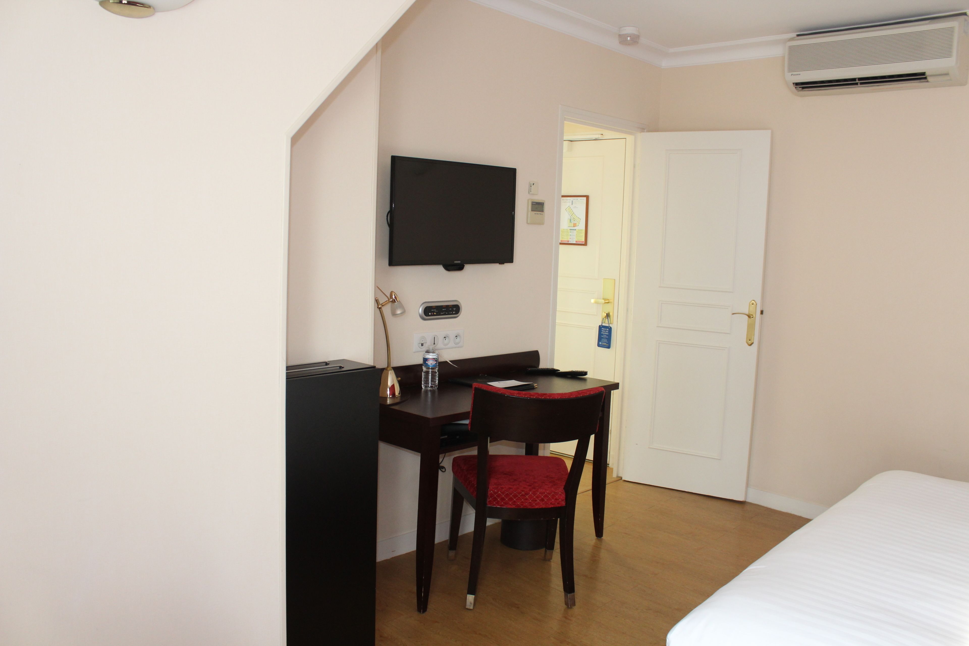 Una habitación de hotel con cama, escritorio con silla, televisor y aire acondicionado.