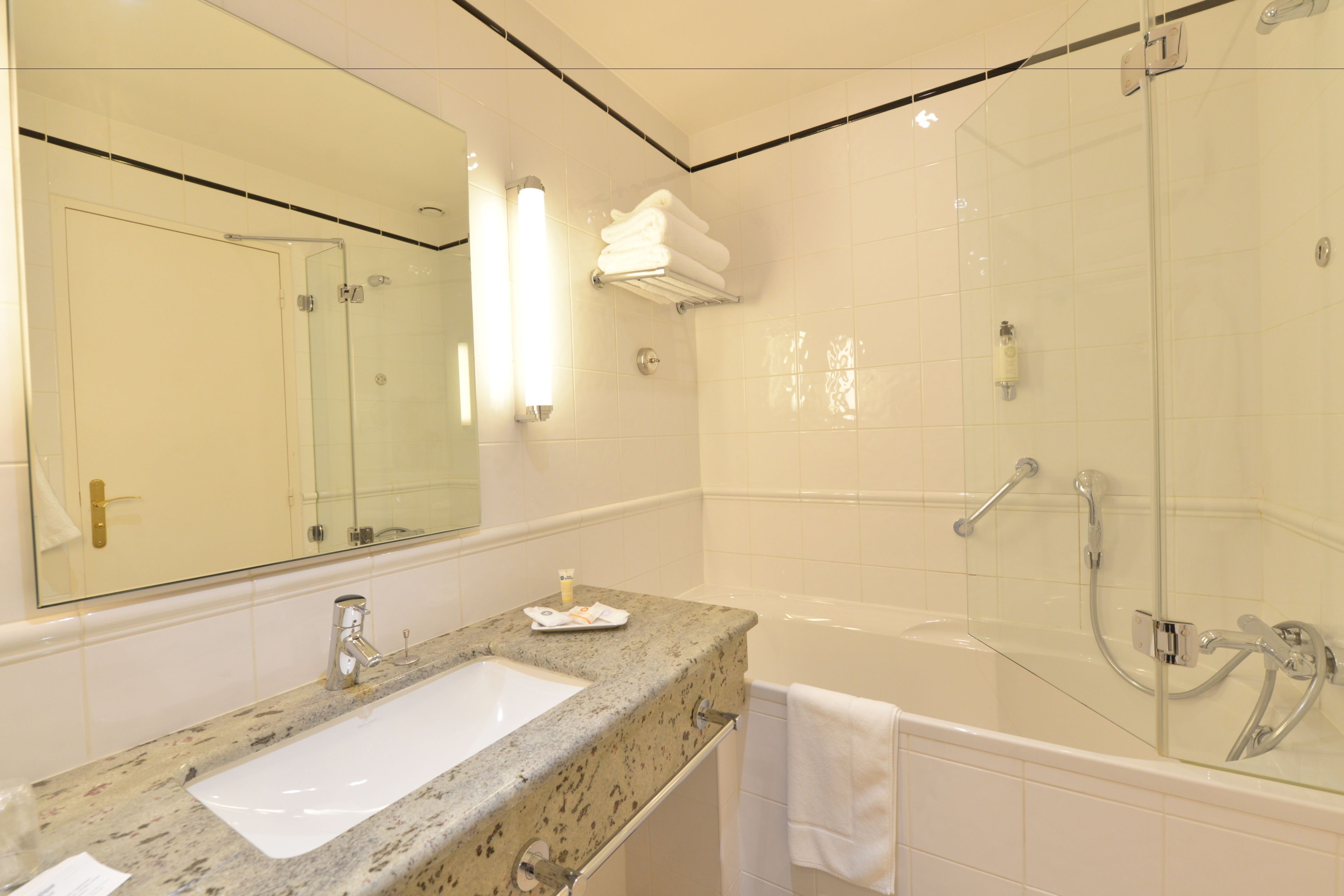 A bathroom with a granite countertop sink, a large mirror, a glass-enclosed shower, and a white towel hanging on the wall.