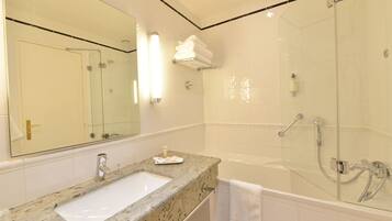 A bathroom with a granite countertop sink, a large mirror, a glass-enclosed shower, and a white towel hanging on the wall.