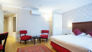A hotel room with a large bed, two red chairs, a small table, and a red rug.