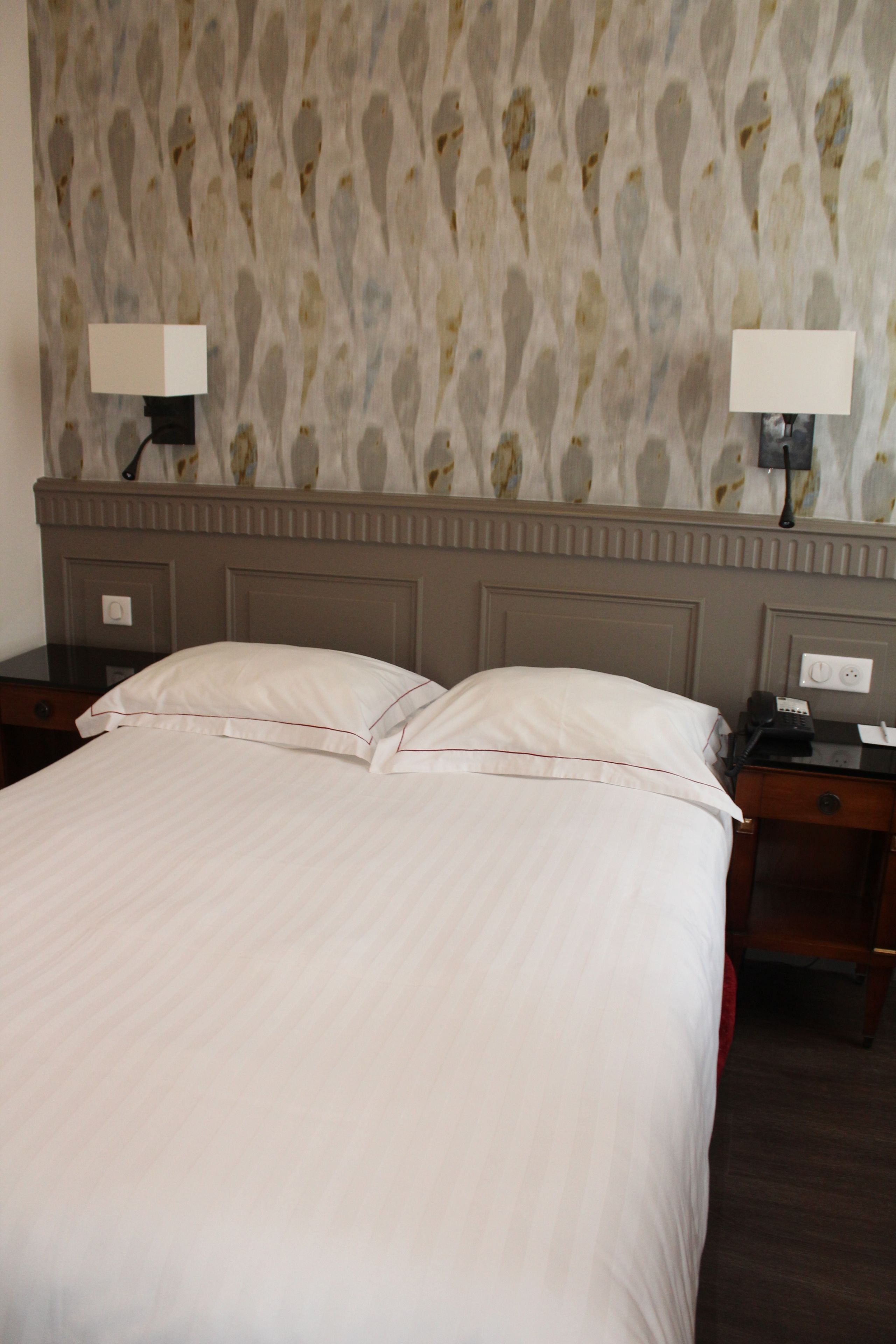 Une chambre d’hôtel avec un grand lit, deux tables de chevet et une tête de lit ornée d’un papier peint à motifs.