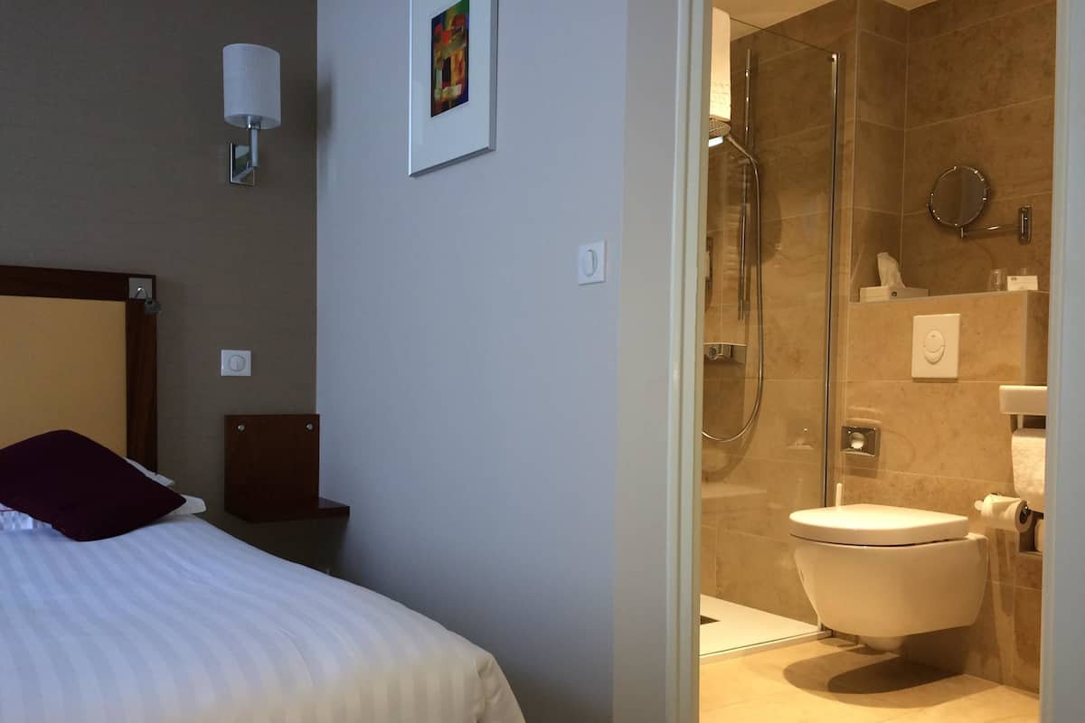 A hotel room with a bed, a shower area, and a toilet.