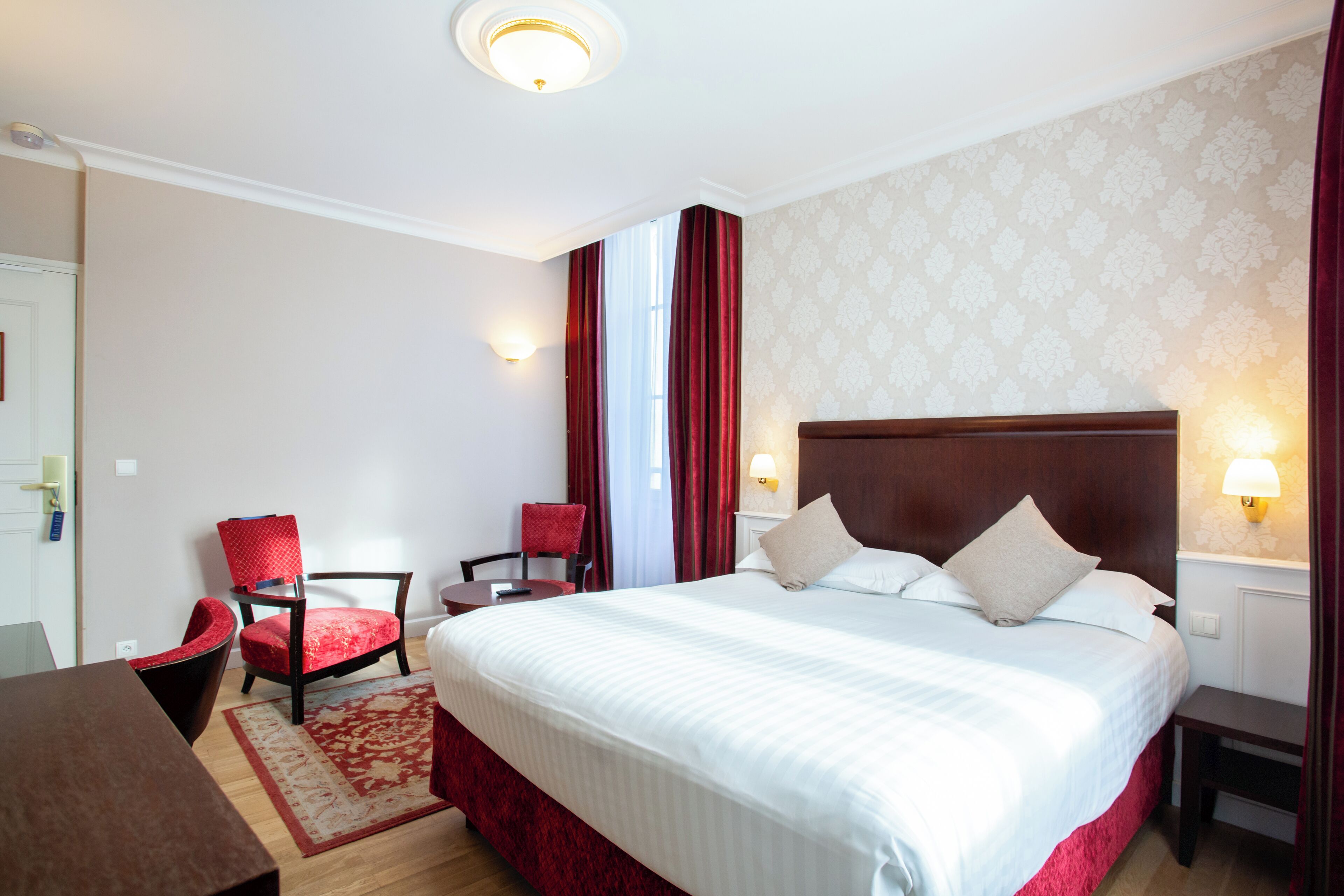 A hotel room with a large bed, two chairs, a desk, and a red accent wall.