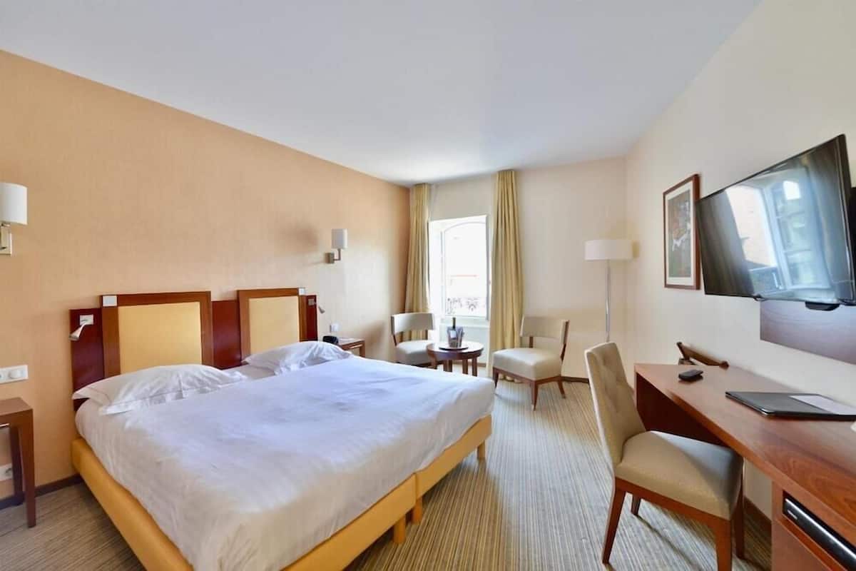 A hotel room with a bed, desk, chair, TV, and lamp.