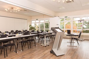 Un salón de conferencias con varias mesas, sillas y una pantalla de presentación.