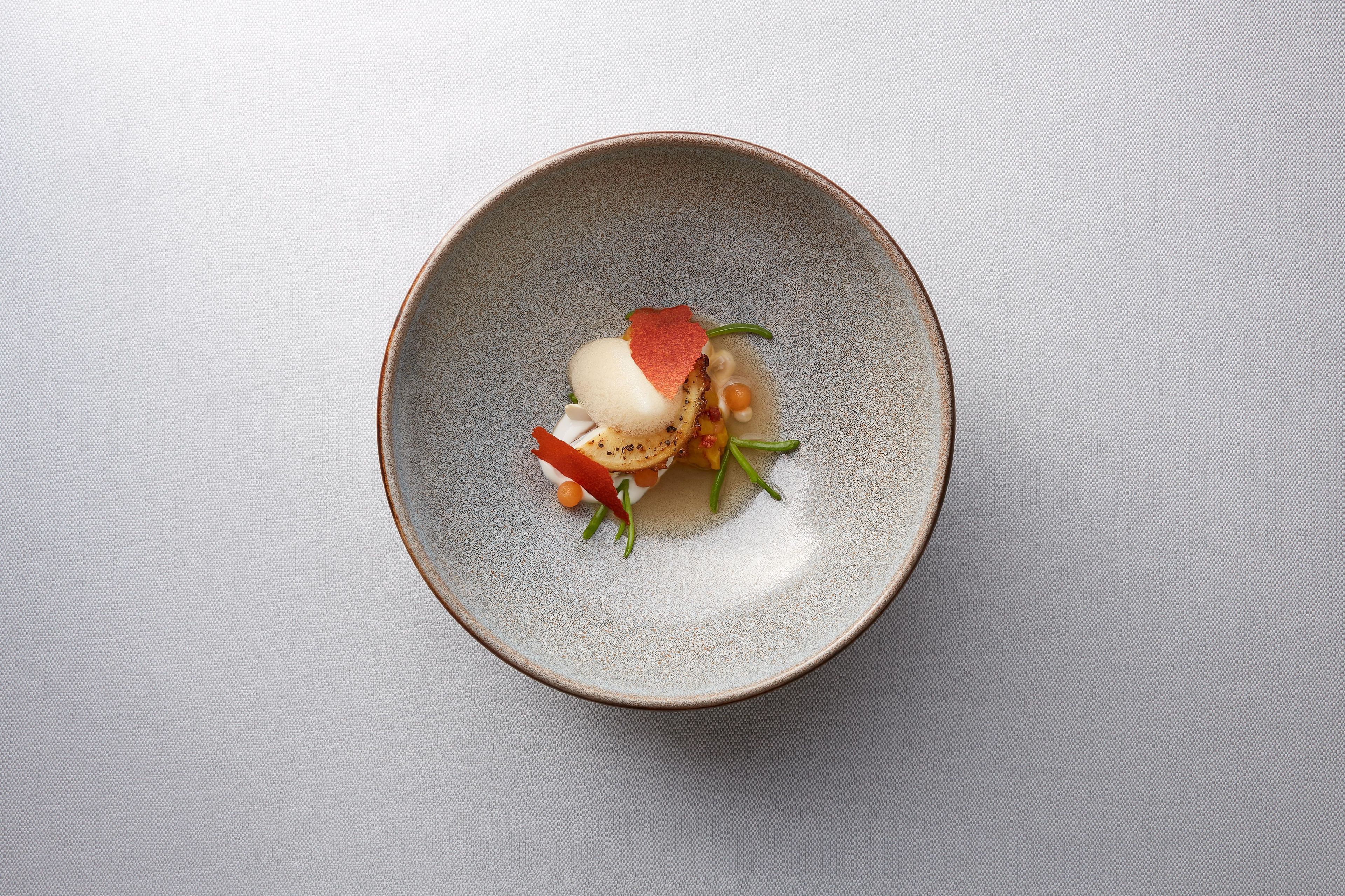Une assiette ronde en céramique, sur laquelle se trouve un plat, posée sur une surface texturée.
