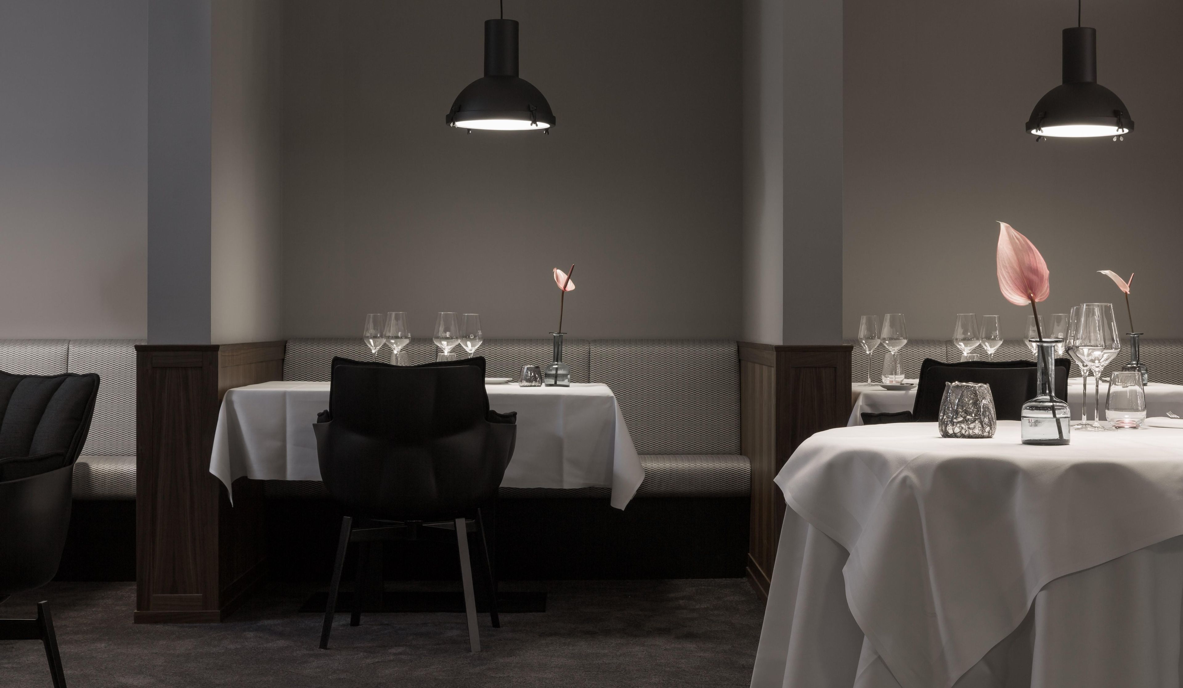 A restaurant interior with tables set for dining, chairs, and pendant lighting.