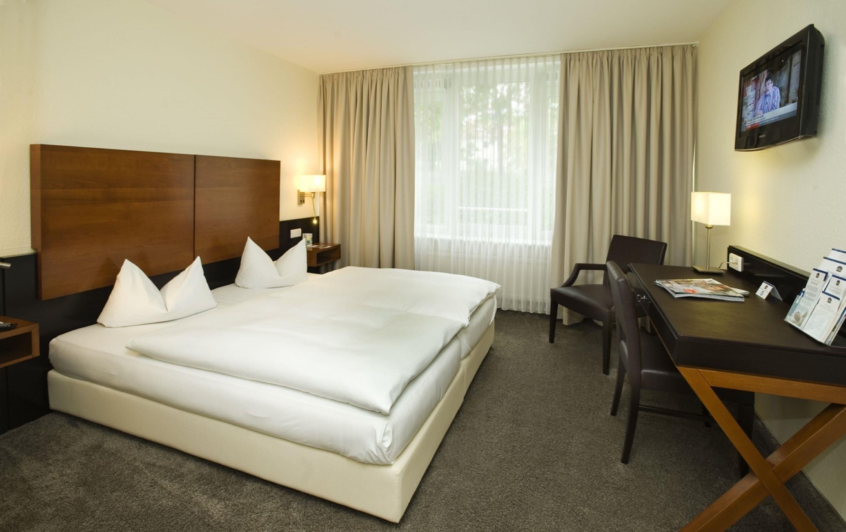 A hotel room with a large bed, a desk, a chair, and a television mounted on the wall.
