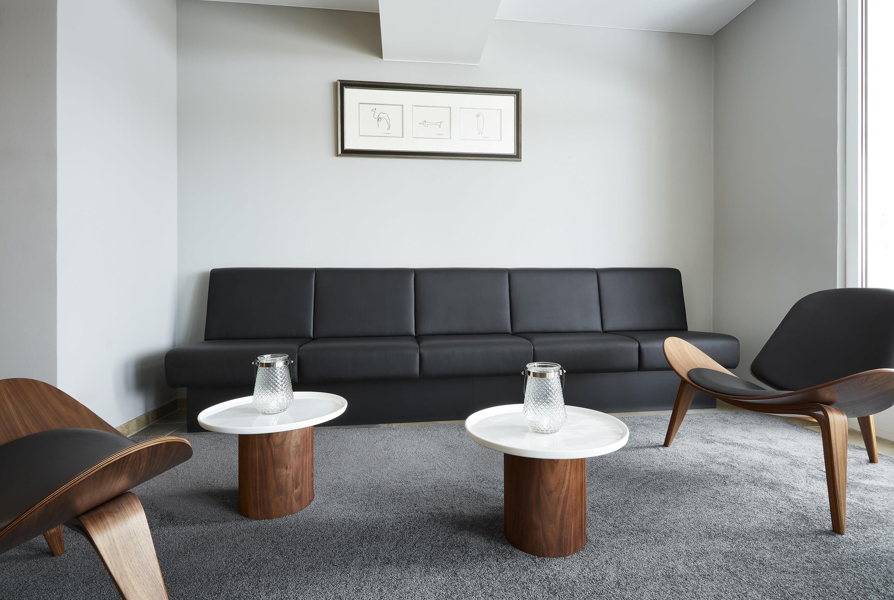 A modern living room with a black sofa, two wooden side tables, and a glass jar on each.