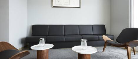 A modern living room with a black sofa, two wooden side tables, and a glass jar on each.