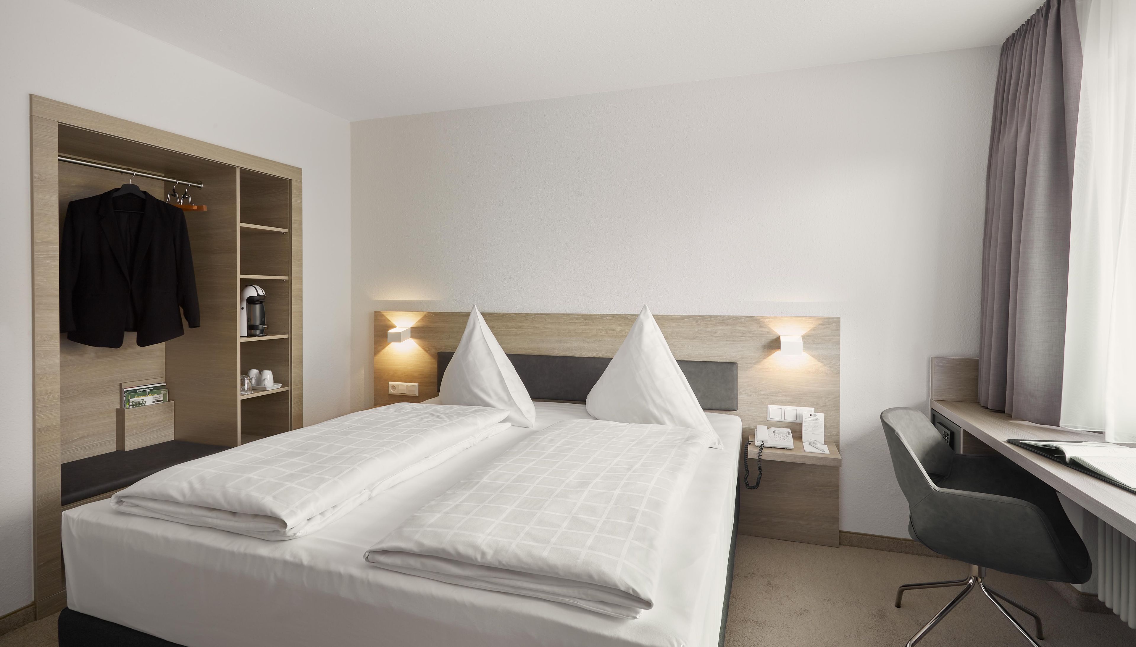 Ein Hotelzimmer mit Bett, Nachttischen, Schreibtisch, Stuhl, Kleiderschrank und einer Kaffeemaschine.