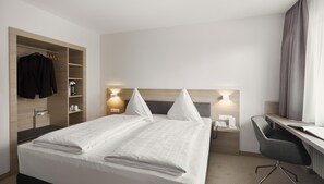 A hotel room with a bed, bedside tables, a desk, a chair, a wardrobe, and a coffee machine. - Scotty + Emily Hotel Ulm, Sure Hotel Collection by BW (Ulm)