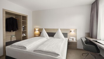 Habitación de hotel con cama, mesitas de noche, escritorio, silla, armario y cafetera.