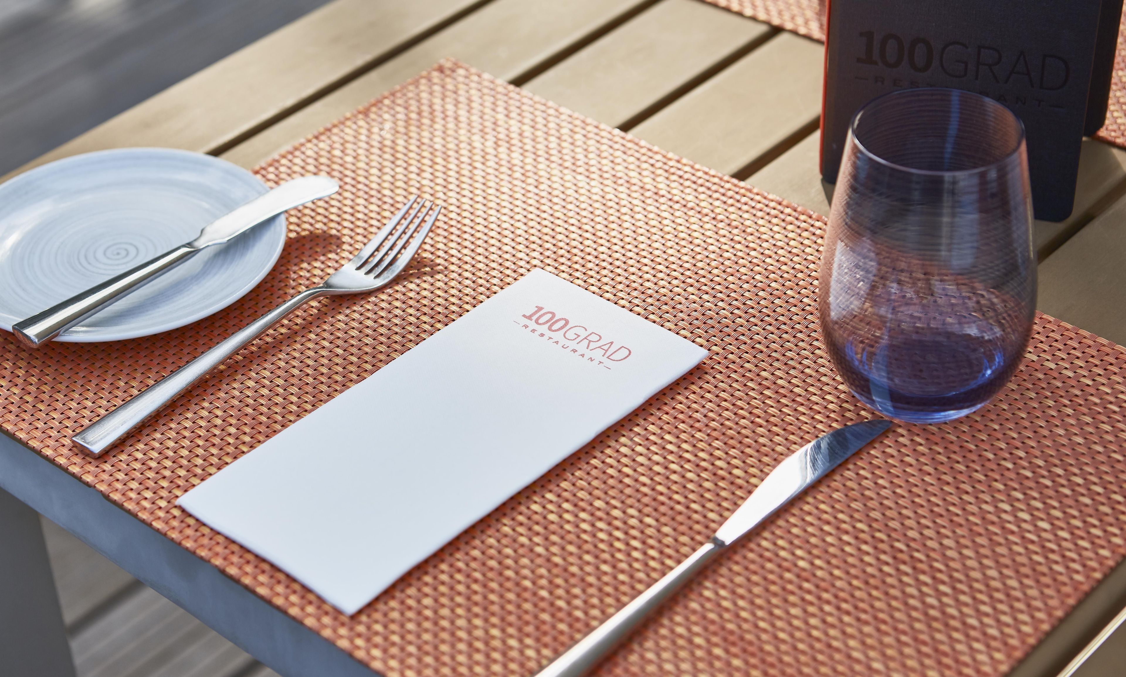 A table set with a white placemat, a glass of water, cutlery, and a plate.