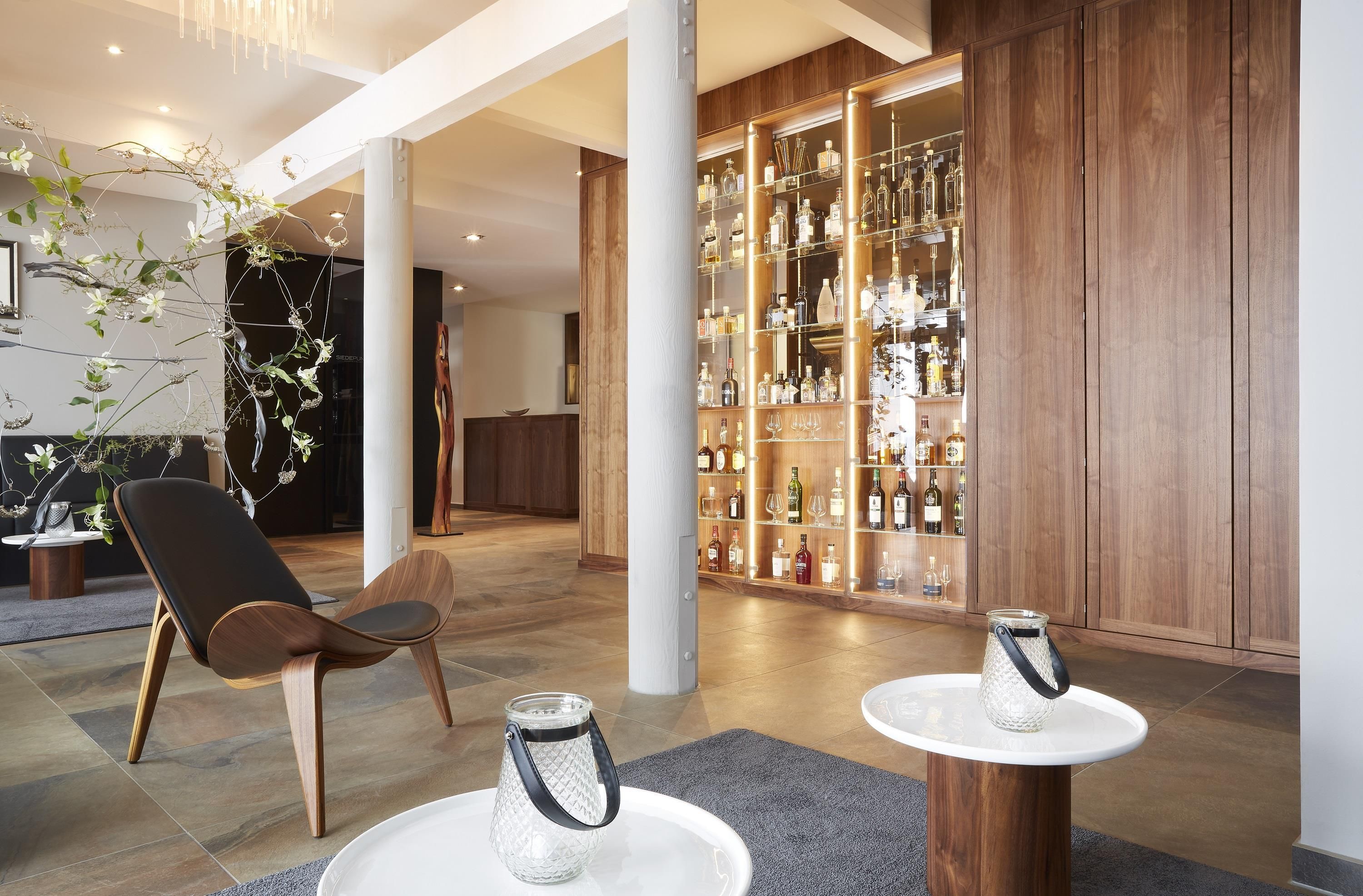 Un interior moderno con zona de bar, suelo de madera y una sala de estar con una silla y mesas.