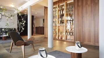 Un interior moderno con zona de bar, suelo de madera y una sala de estar con una silla y mesas.