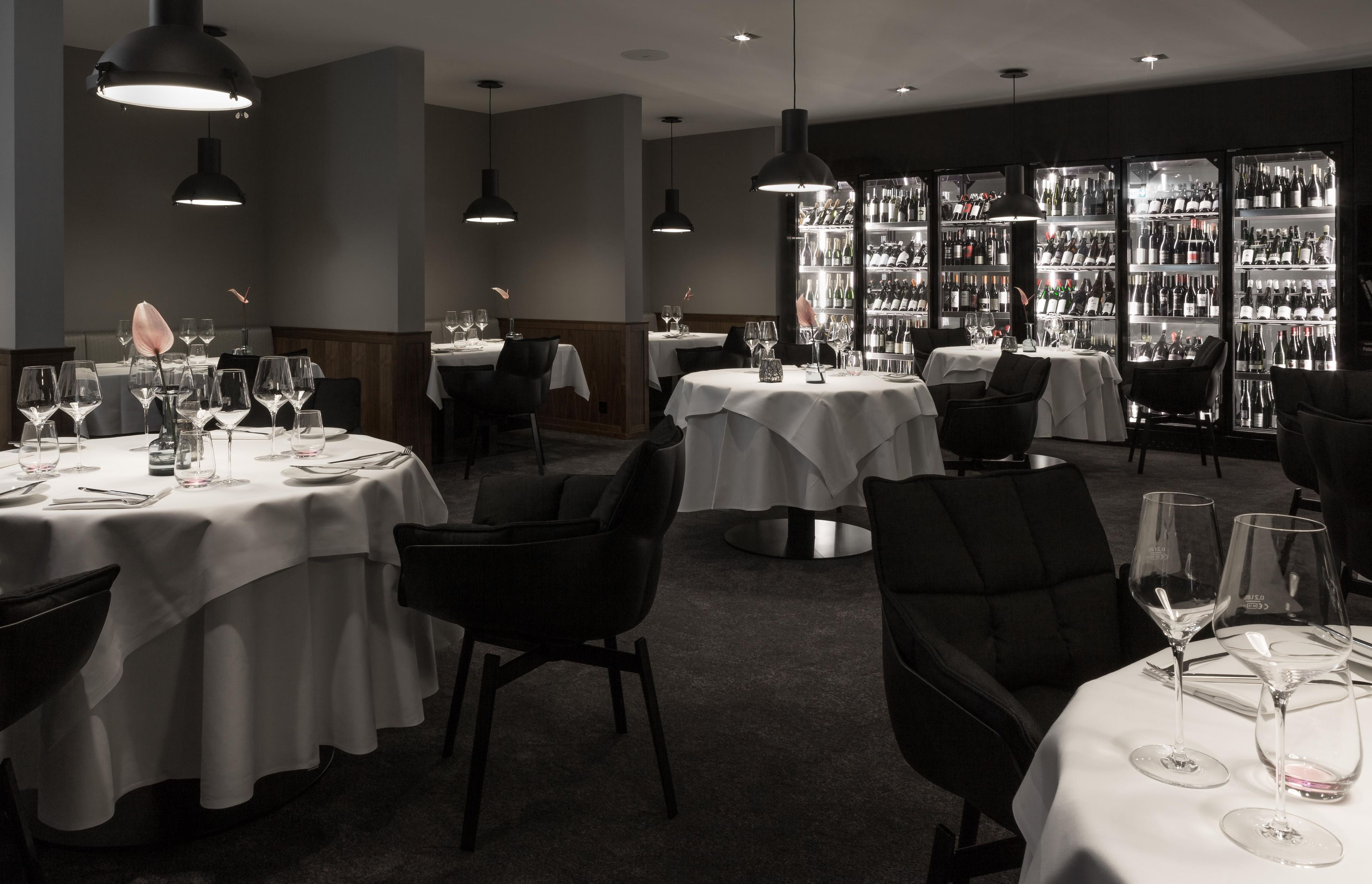 Ein Restaurant mit runden Tischen, schwarzen Stühlen und Pendelleuchten.