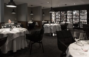 Un restaurante con mesas redondas, sillas negras e iluminación colgante.