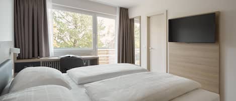A hotel room with two beds, a desk, a television, and a window with curtains.