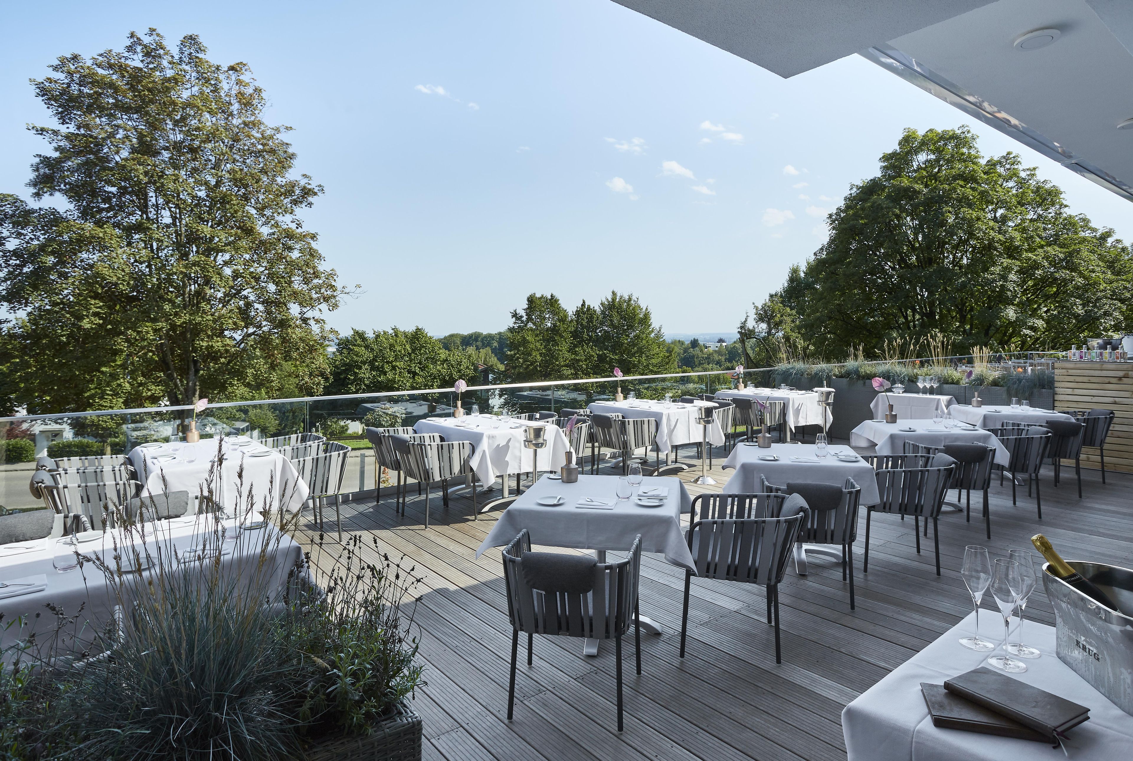 Un área de comedor al aire libre con varias mesas y sillas, rodeada de vegetación y árboles.