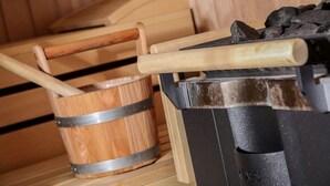 Una sauna con bancos de madera, un balde de madera y un calentador de sauna negro.