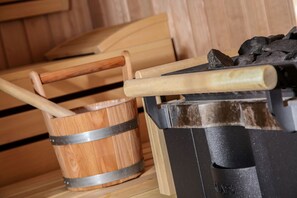 Una sauna con bancos de madera, un balde de madera y un calentador de sauna negro.