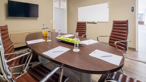 Una sala de conferencias con una mesa redonda, sillas de cuero marrón, un televisor de pantalla plana, una pizarra y una puerta.