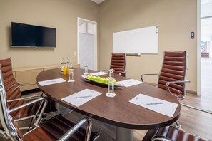 Una sala de conferencias con una mesa redonda, sillas de cuero marrón, un televisor de pantalla plana, una pizarra y una puerta.