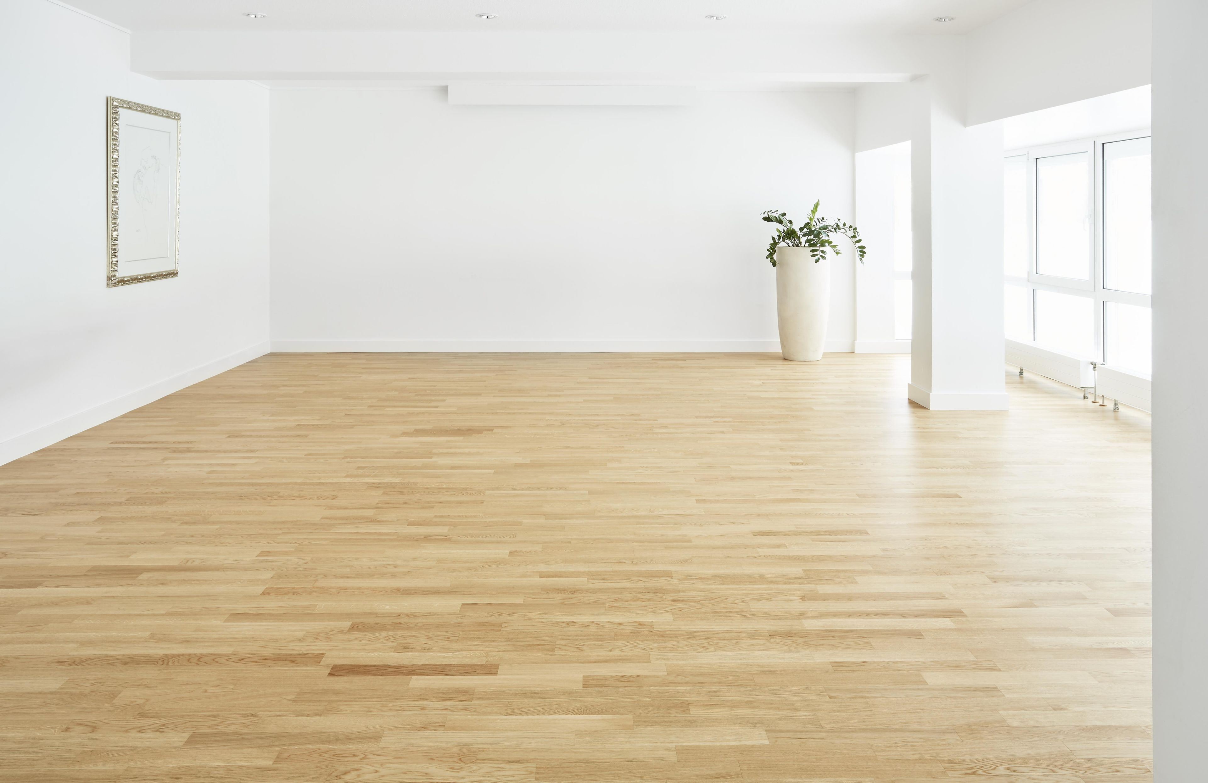 Una habitación amplia con piso de madera, paredes blancas y un gran ventanal.