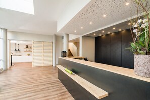 Un área de recepción moderna con un mostrador de madera, una planta en maceta y una escalera al fondo.