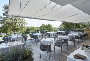 Un área de comedor al aire libre con mesas y sillas, cubierta por un toldo, rodeada de follaje.