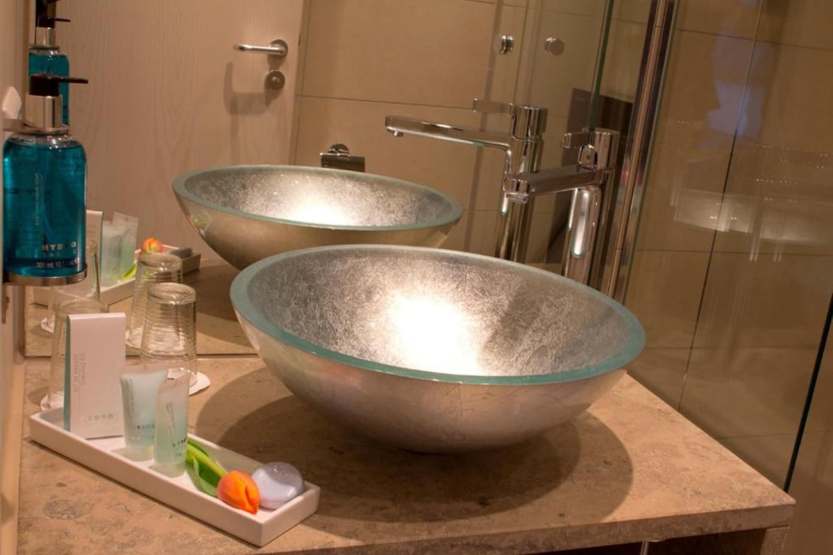 Un baño con dos grandes cuencos de vidrio como lavamanos, una botella azul y una bandeja con artículos de aseo.