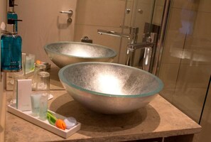 Un baño con dos grandes cuencos de vidrio como lavamanos, una botella azul y una bandeja con artículos de aseo.