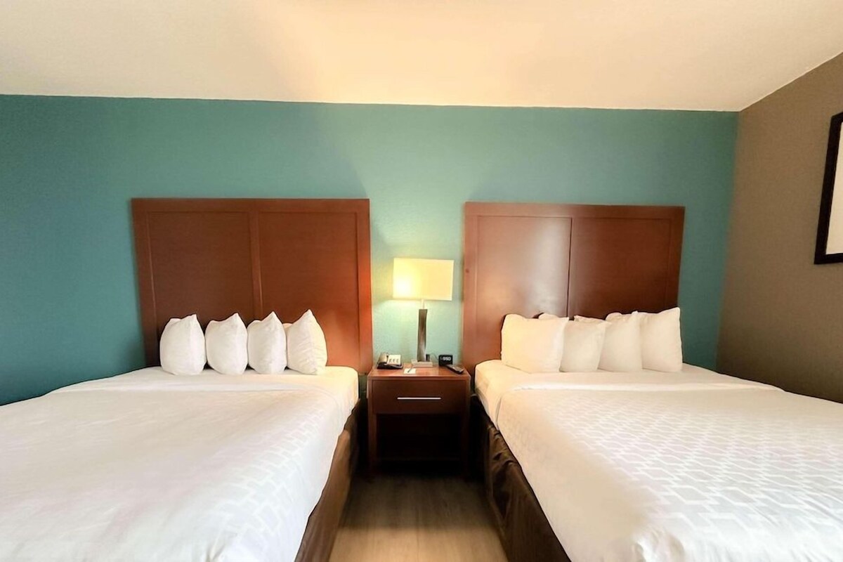A hotel room with two beds, a nightstand with a lamp, and teal walls.