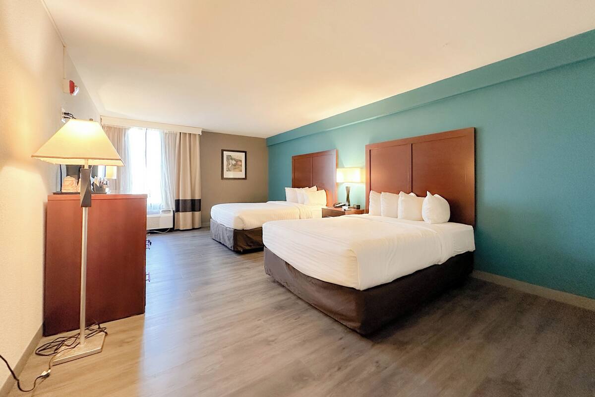 A hotel room with two beds, a desk, and a lamp.