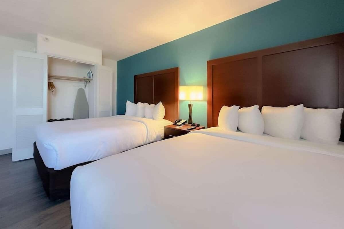 A hotel room with two beds, a wardrobe, and a bedside table with a lamp.