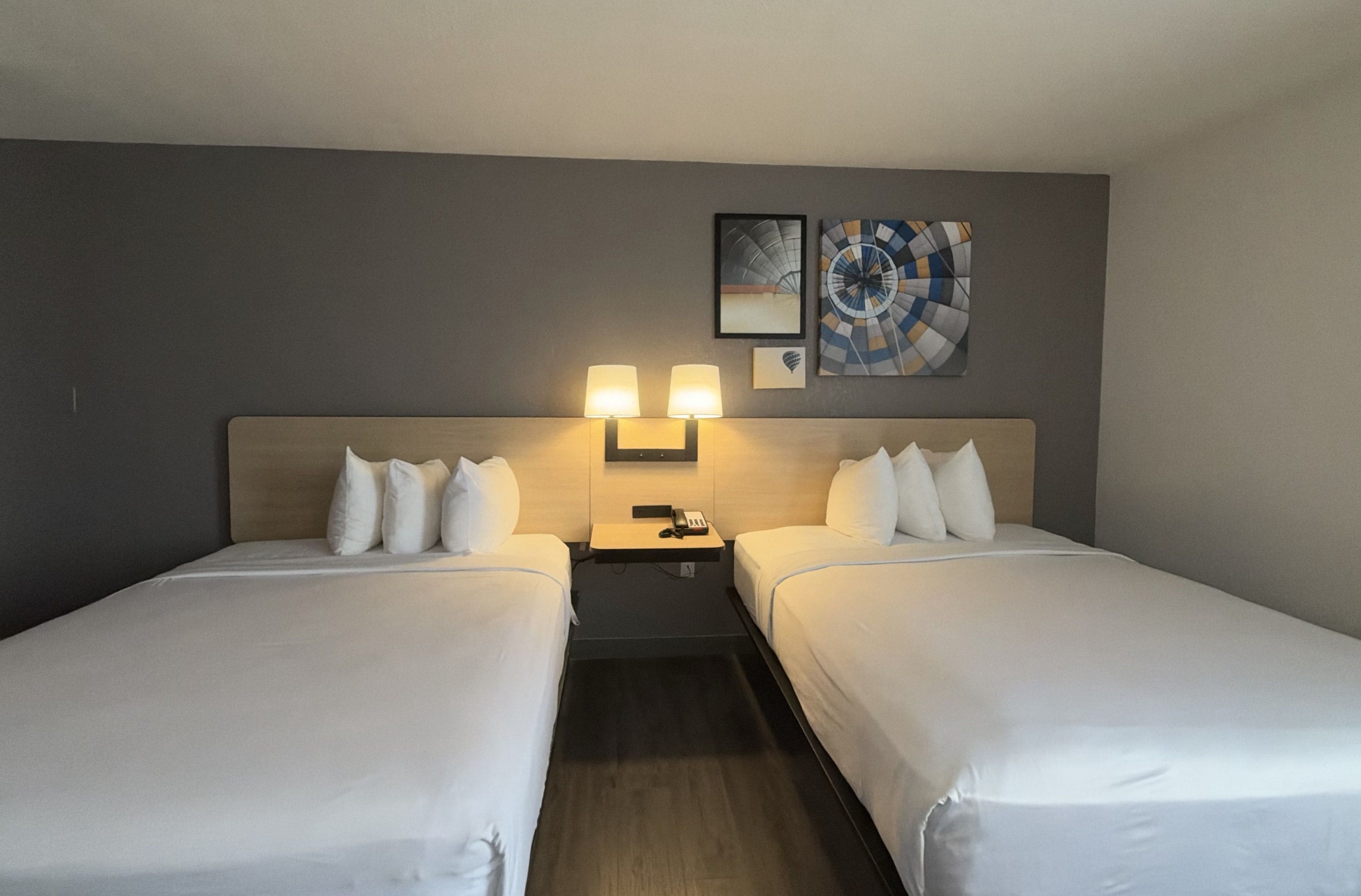 A hotel room with two single beds, a nightstand with a lamp, and two wall-mounted lamps.