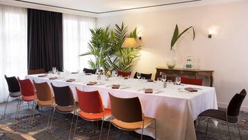 A conference room with a long table set for a meeting, surrounded by chairs, a plant, and a lamp.