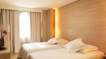 A hotel room with two beds, a desk, a lamp, and a window with curtains.