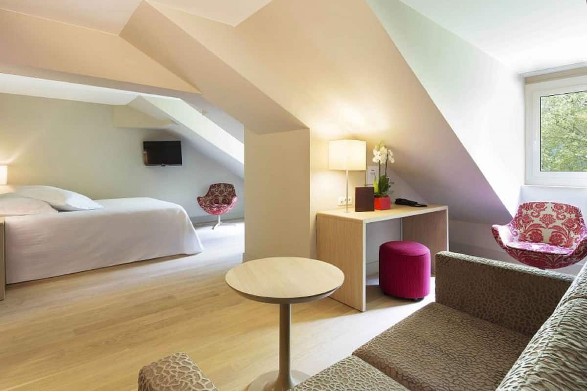A modern hotel room with a lofted sleeping area, a small round table, a sofa, and a chair.