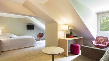 Ett modernt hotellrum med en sovplats på ett övre plan, ett litet runt bord, en soffa och en stol.