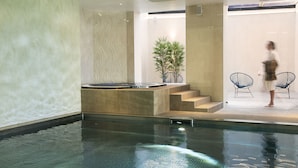 An indoor swimming pool with a stone wall, a staircase, and a seating area with chairs. - Oceania L'Univers Tours (Tours)