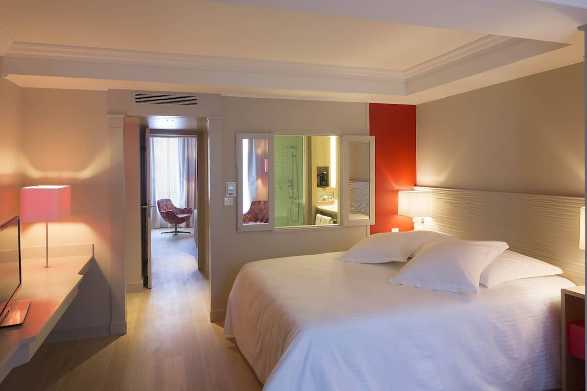 A hotel room with a bed, bedside lamps, a mirror, and a view of the bathroom.