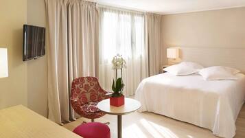 Una habitación de hotel con una cama, una silla, una mesita con una planta y un televisor montado en la pared.