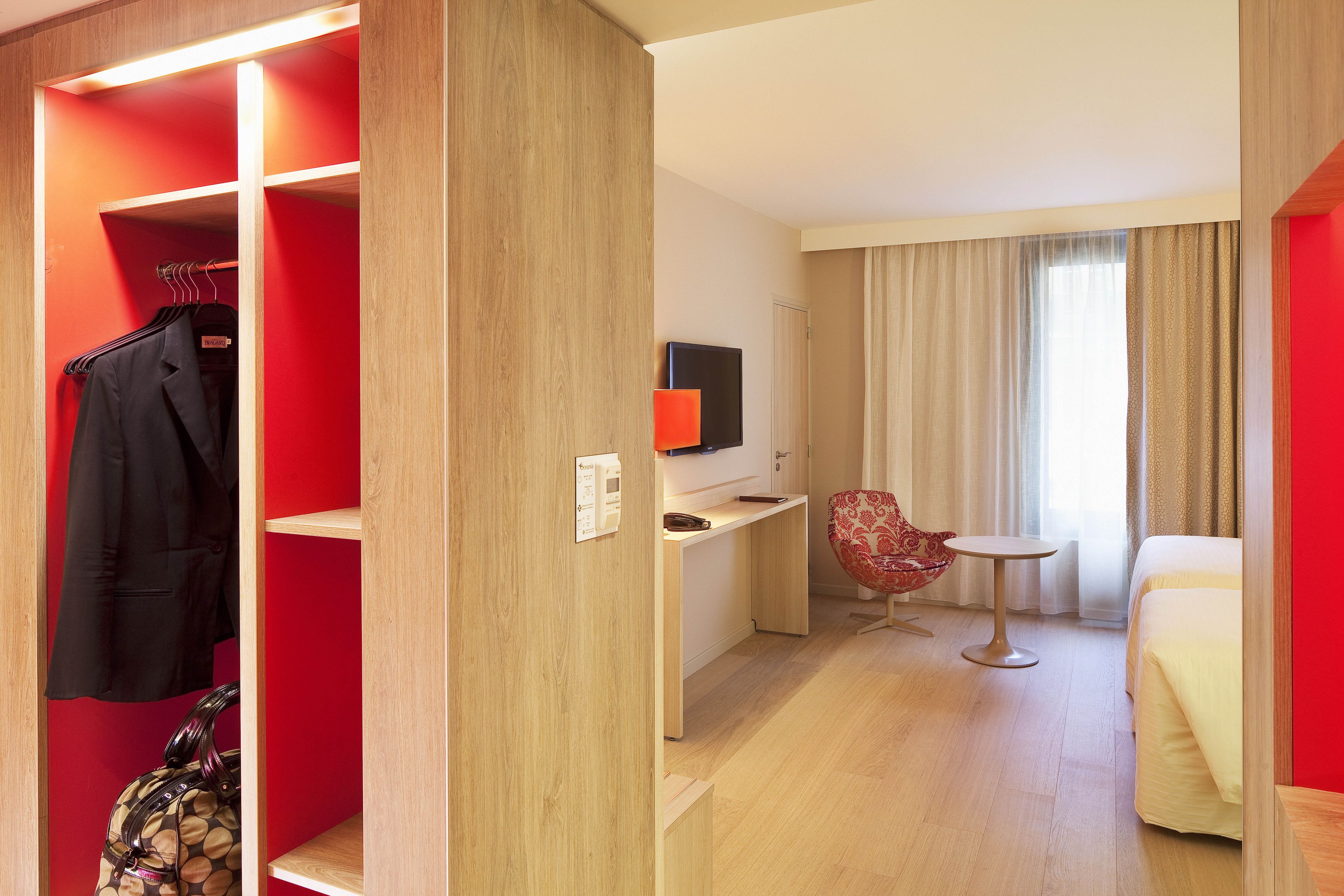 Quarto de hotel com uma cama, escrivaninha, cadeira, televisão e guarda-roupa.
