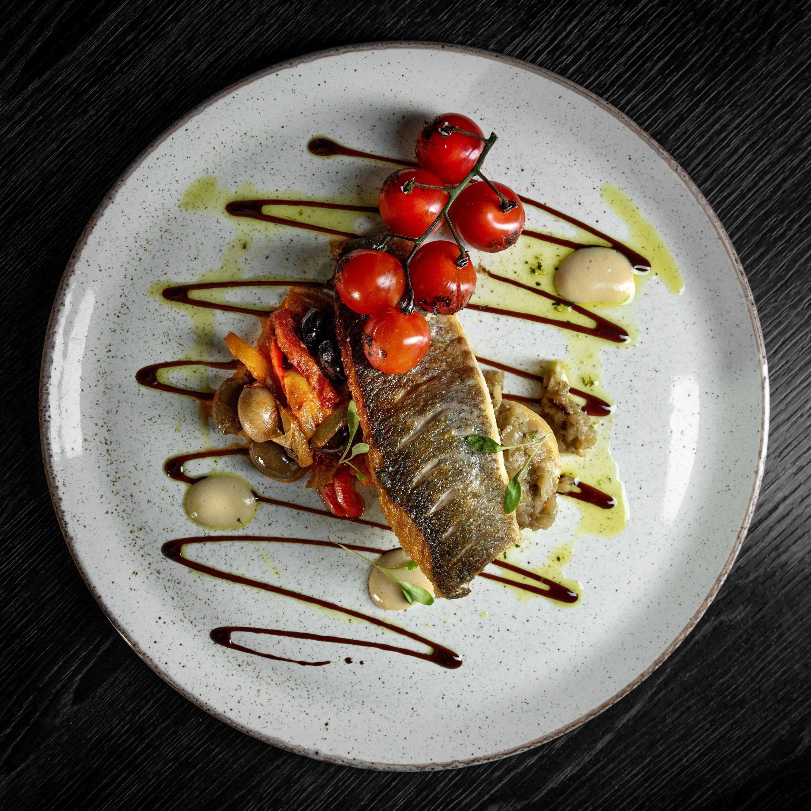 A plate of food with a fish, cherry tomatoes, and vegetables.