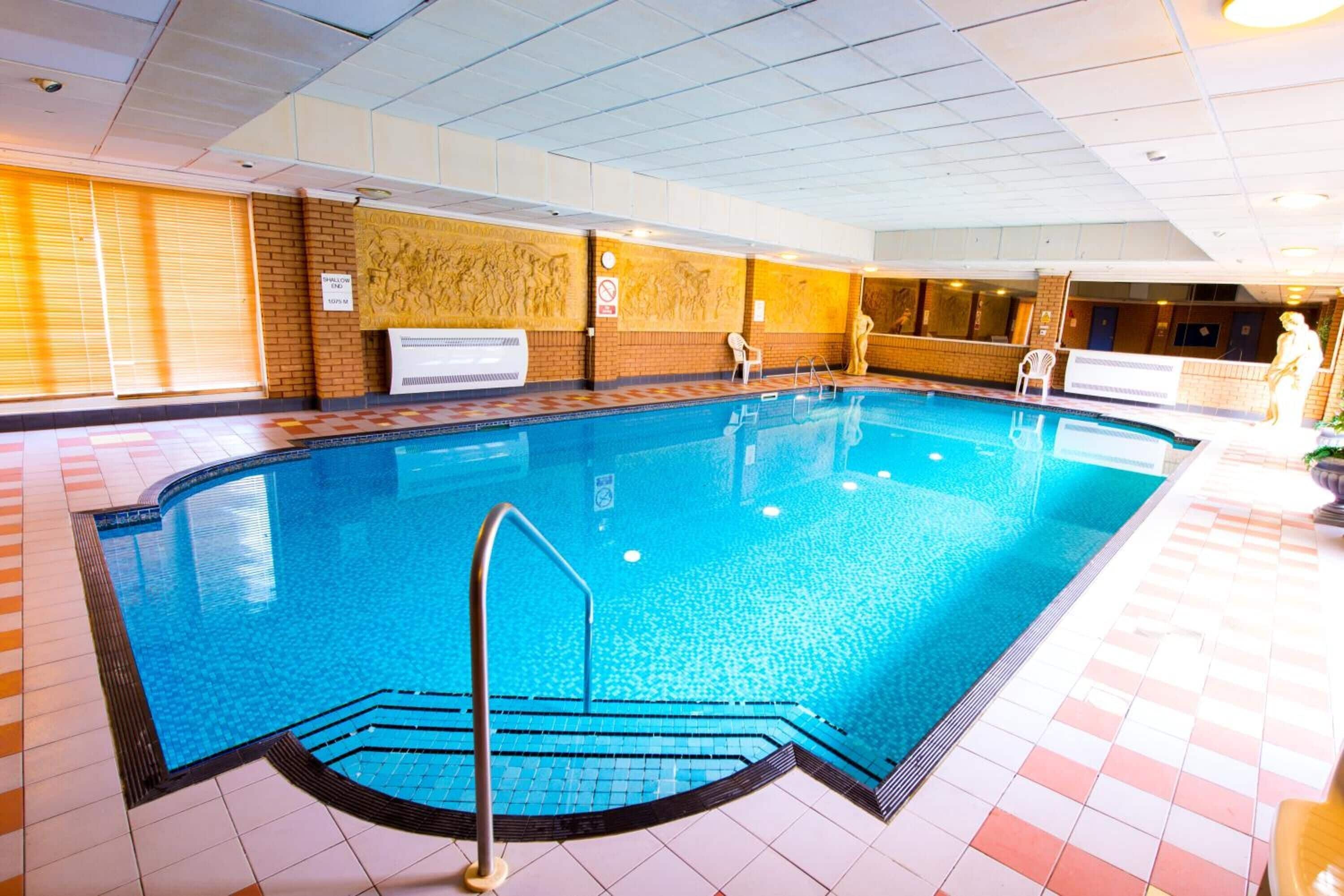 An indoor swimming pool with clear water, tiled floor, and a lifeguard stand.