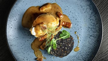 A plate with a dark-colored patty, a piece of meat, and a creamy sauce.