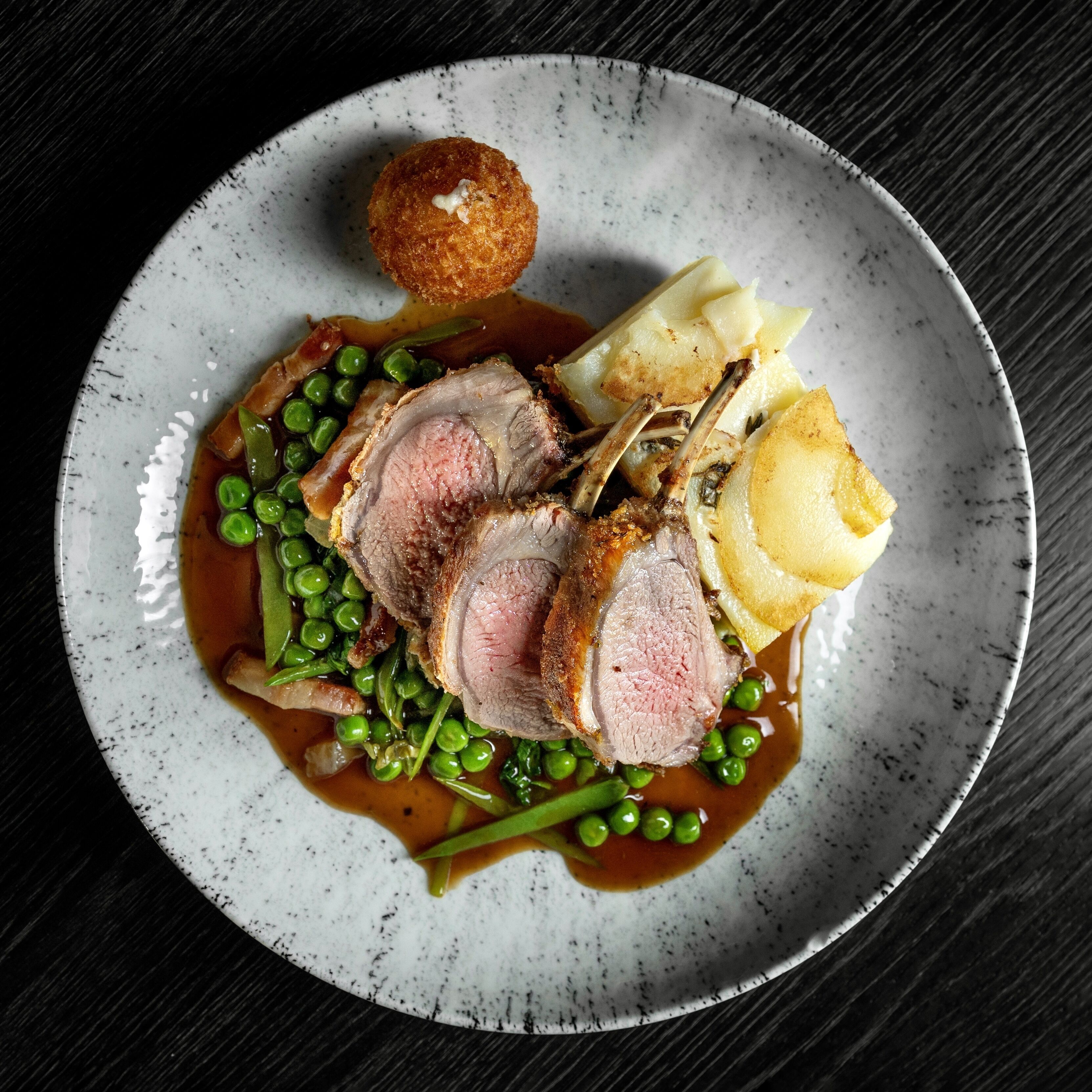 A plate with sliced meat, peas, mashed potatoes, and a small round item, possibly a dumpling, on a speckled ceramic plate.